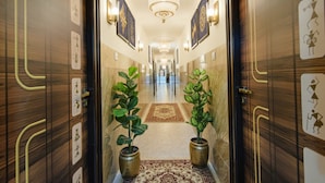 Un couloir d’hôtel avec des portes en bois, des œuvres d’art encadrées et des plantes en pot.