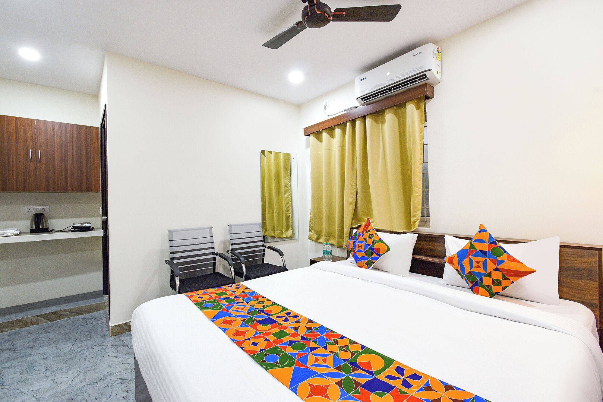 A hotel room with a bed, a desk, a chair, a ceiling fan, and an air conditioning unit.