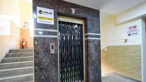 Un ascenseur doté d’un écran numérique, d’un extincteur et d’un panneau indiquant les heures d’arrivée et de départ à l’hôtel Elite Inn.