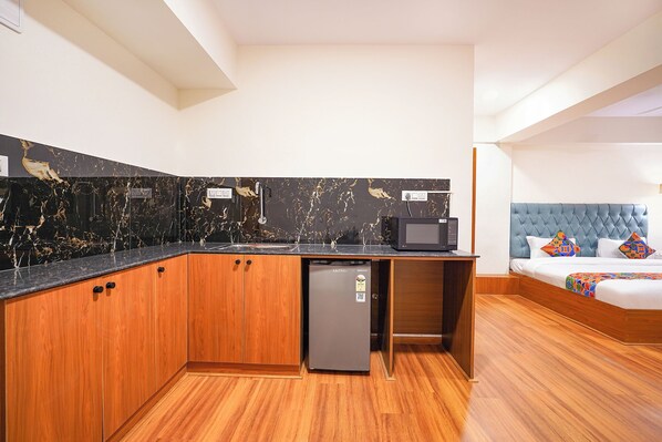 Habitación de hotel compacta con kitchenette, una cama con cabecera acolchada y un refrigerador pequeño.