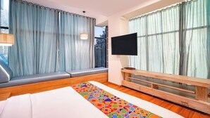 Una camera d'albergo moderna con un letto grande, una TV a parete e una finestra con tende.