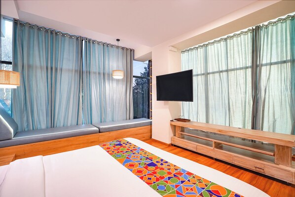Una habitación de hotel moderna con una cama grande, un televisor montado en la pared y una ventana con cortinas.