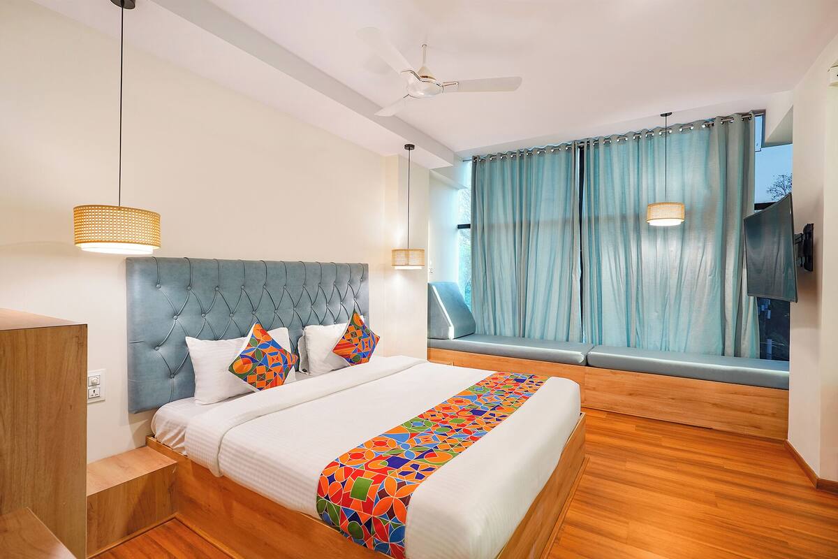 Una habitación de hotel moderna con una cama grande, un ventanal con cortinas, un ventilador de techo y suelo de madera.