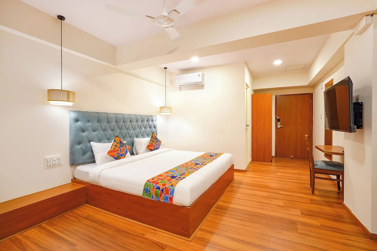 Habitación de hotel con una cama grande, ventilador de techo, aire acondicionado, televisor y piso de madera.