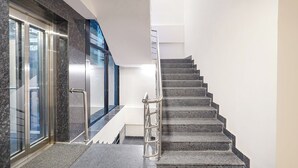 Una moderna scala con ringhiera in metallo, che conduce a un pianerottolo con una porta in vetro e vista sull'esterno.