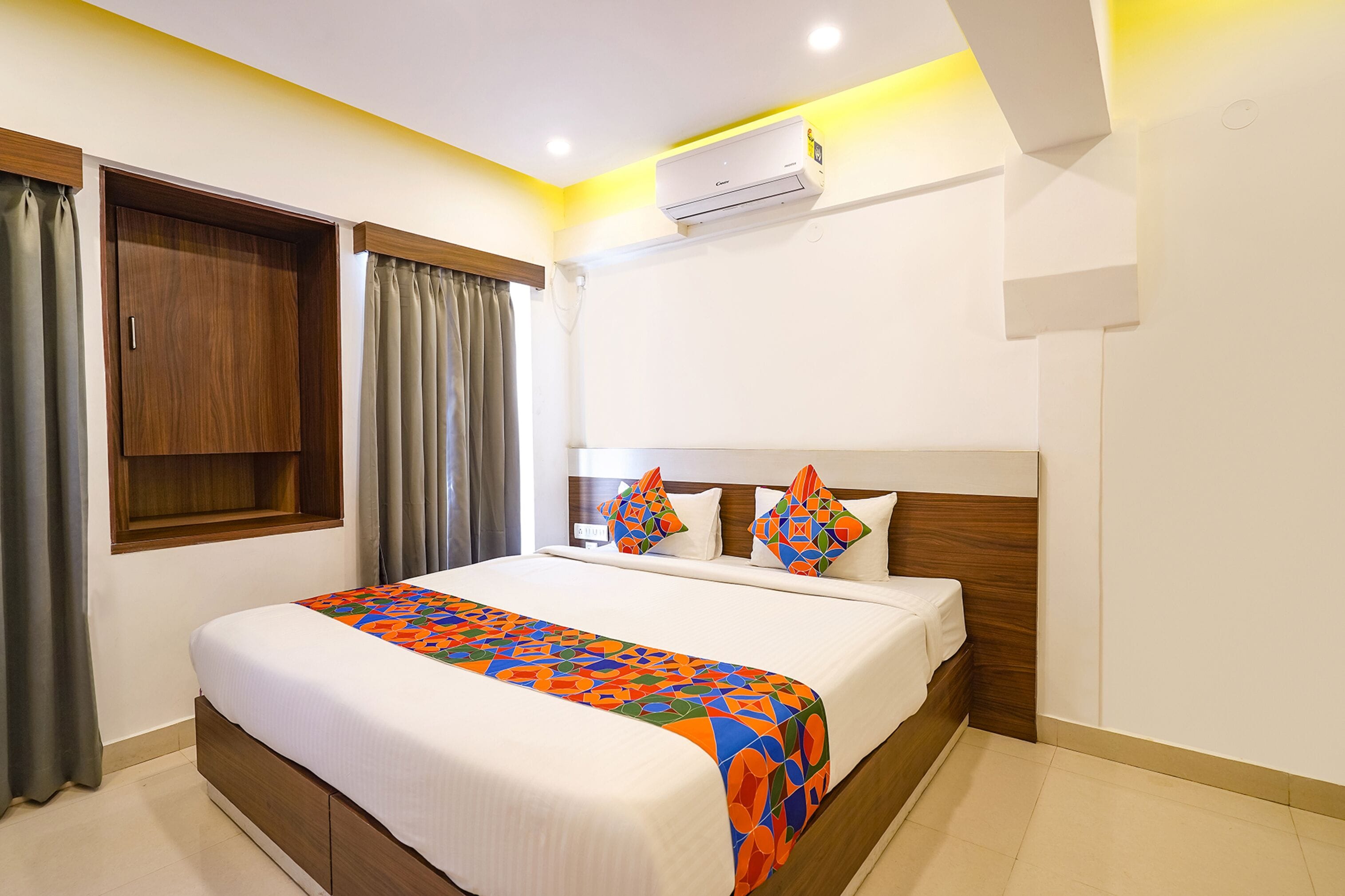 A hotel room with a bed, curtains, an air conditioning unit, and a window.