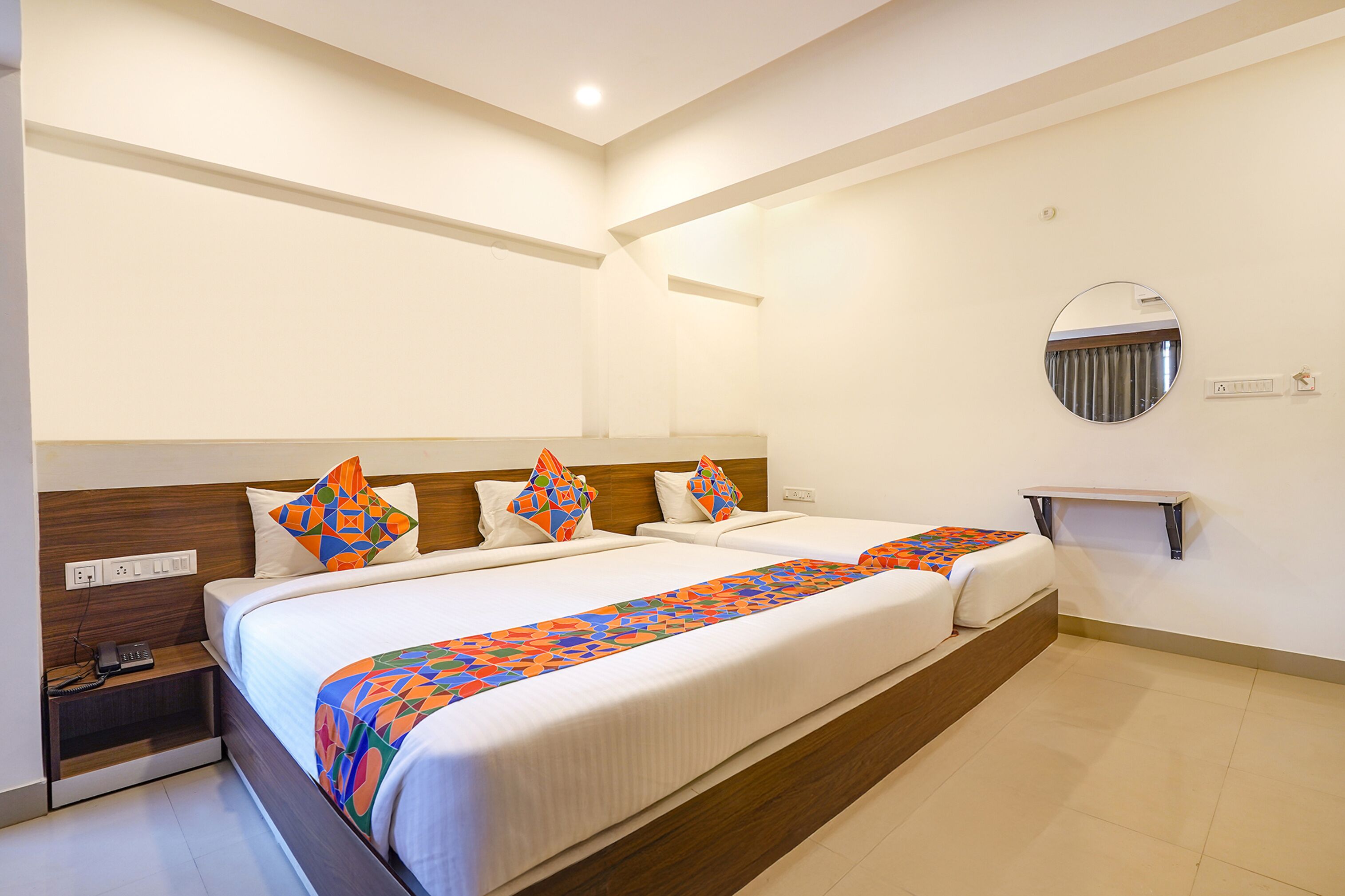 Una habitación de hotel con dos camas, una mesita de noche, un espejo y un pequeño estante.