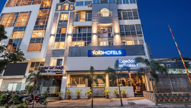 A multi-story hotel with a 'fabHOTELS' sign, a restaurant named 'One Door Restaurant', and several potted plants in front. - FabHotel Royal N Comforts (Bengaluru)
