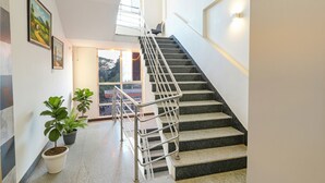 A staircase with metal railings leading to an upper floor, potted plants on the landing, and a view of the outside through a door. - FabHotel Royal N Comforts (Bengaluru)