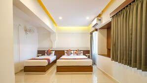 A modern hotel room with two beds, a ceiling fan, an air conditioning unit, and a large window with curtains. - FabHotel Royal N Comforts (Bengaluru)