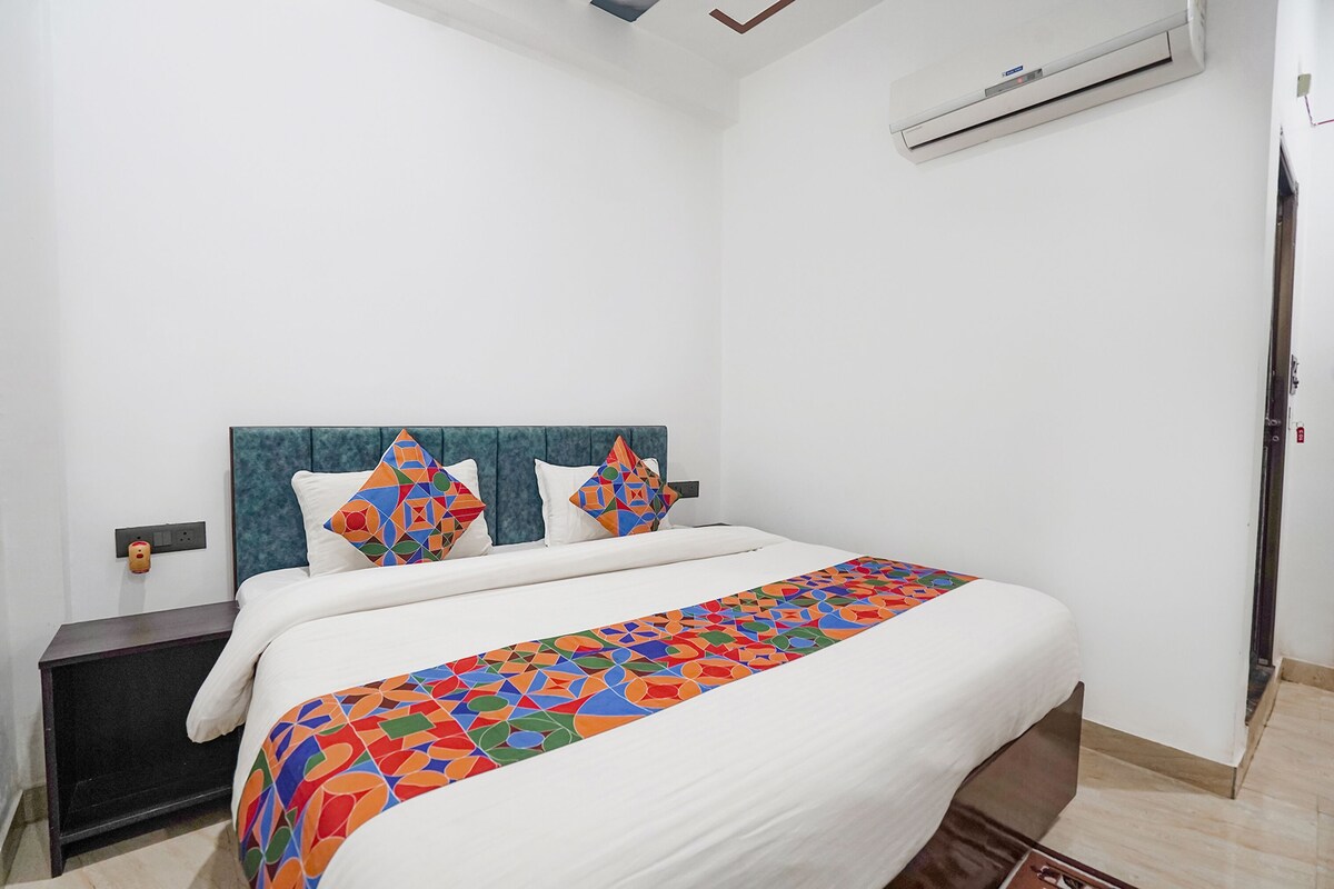 A neatly made bed with a colorful geometric-patterned bedspread, a blue upholstered headboard, and two decorative pillows.
