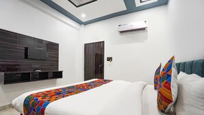 A modern hotel room with a large bed, a flat-screen TV mounted on the wall, an air conditioning unit, and a door with a handle. - Fabhotel The Oak Tree (Faizabad)