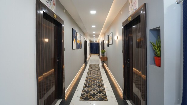 A hotel hallway with dark wooden doors, a patterned carpet, and framed artwork on the walls. - Fabhotel The Oak Tree (Faizabad)
