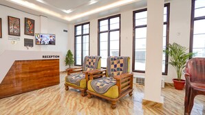 A reception area with a reception desk, two patterned armchairs, a potted plant, and large windows. - Fabhotel The Oak Tree (Faizabad)