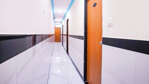 Un long couloir étroit doté d’un sol en marbre, de murs blancs et de moulures noires et brunes. Des portes se trouvent sur le côté droit, et le plafond est agrémenté d’une touche de couleur bleue.