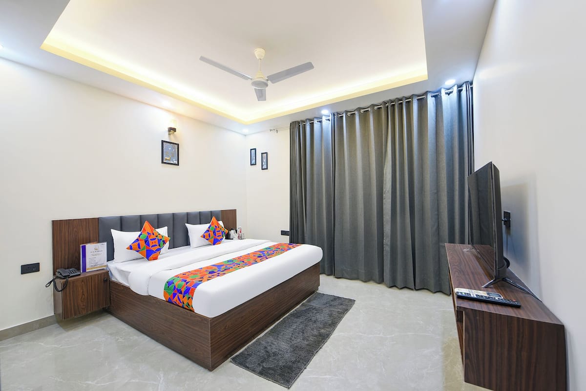 A modern hotel room with a large bed, a desk, a television, and a ceiling fan.