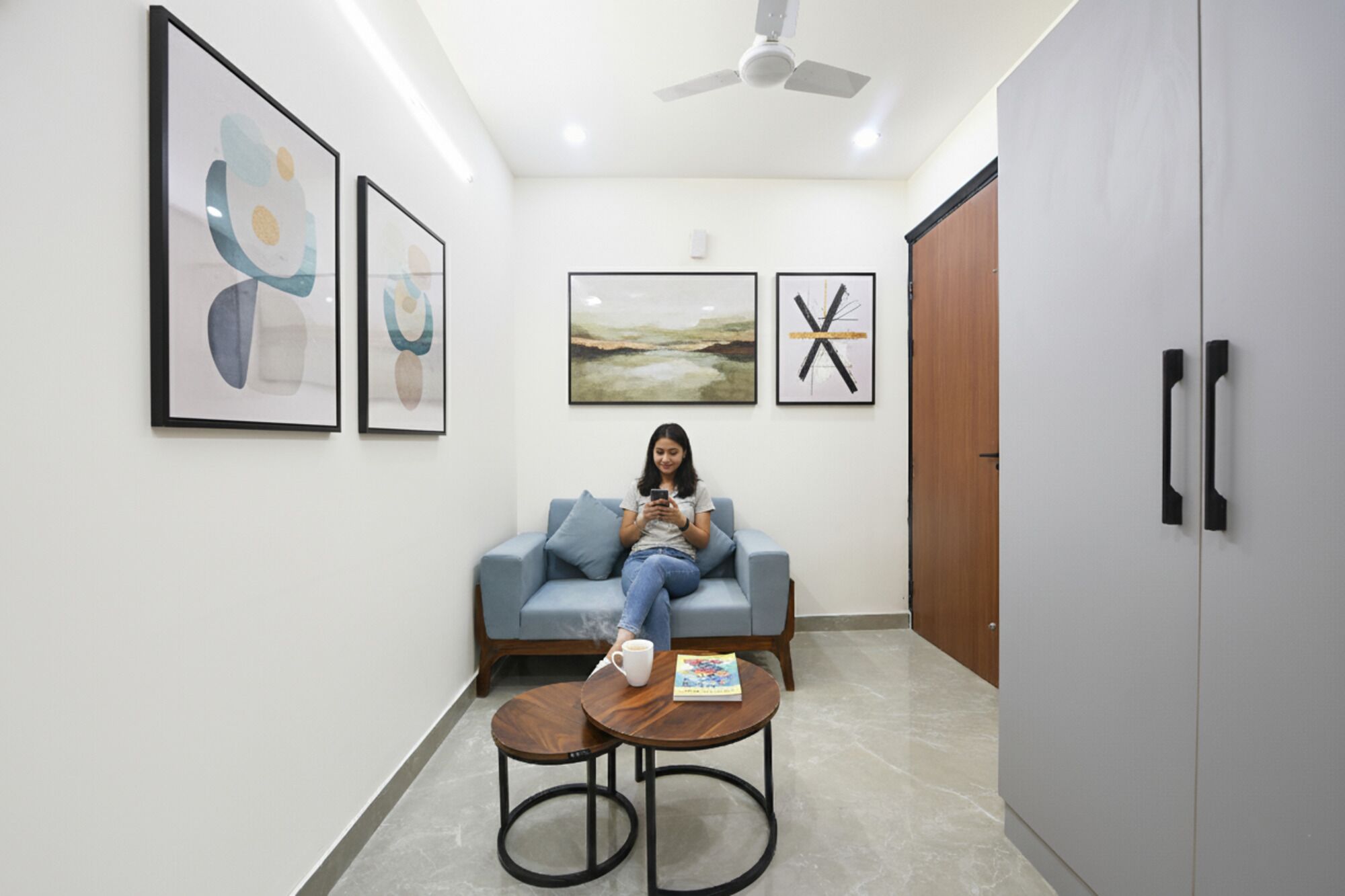 A modern waiting area with a blue sofa, two wooden tables, and artwork on the walls.