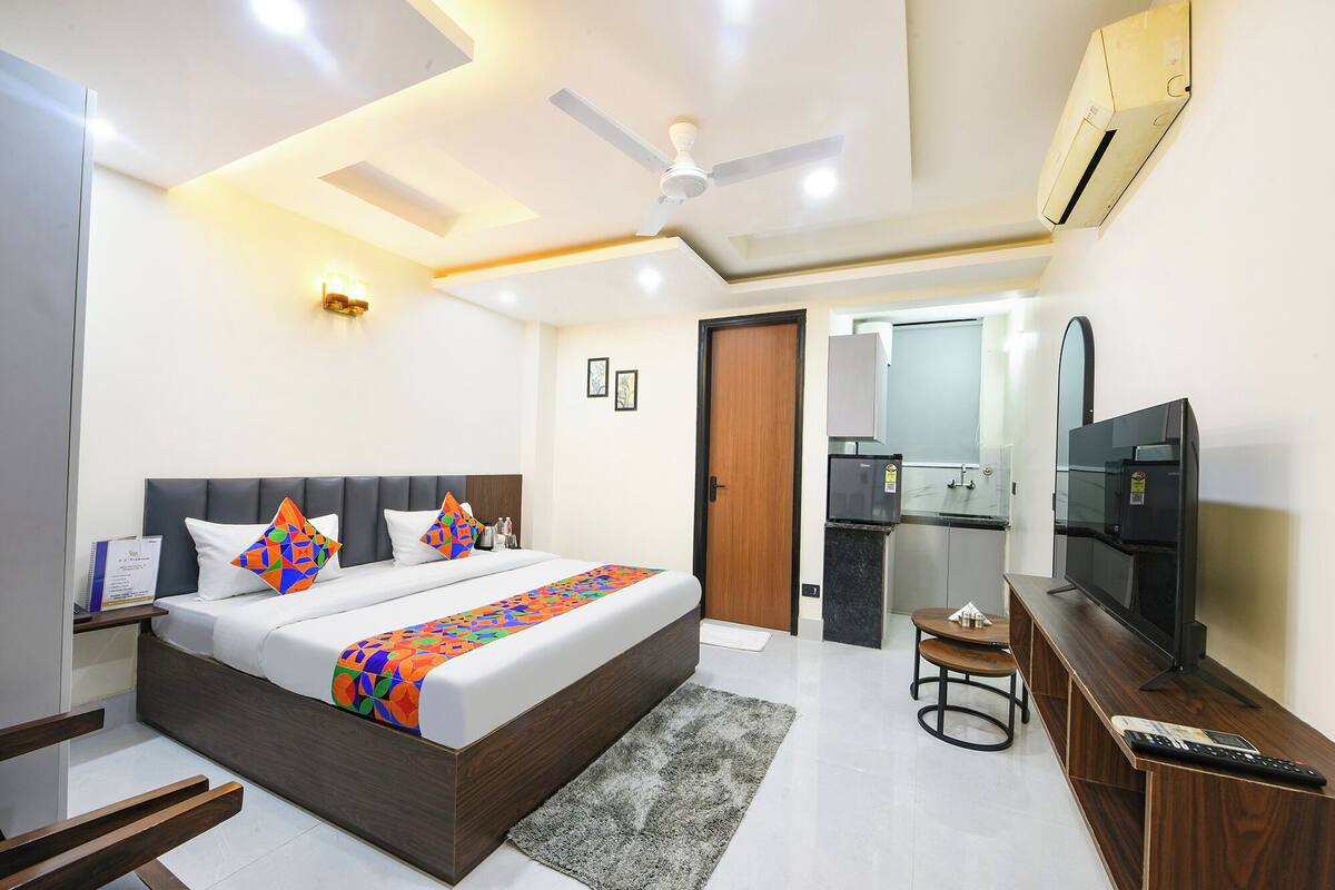Habitación de hotel moderna con una cama grande, televisor, escritorio y baño visible a través de una puerta abierta.