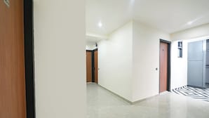 A hallway with a marble floor, a wooden door on the left, and a black and white patterned area rug on the right. - FabHotel RR Premium (Gurugram)