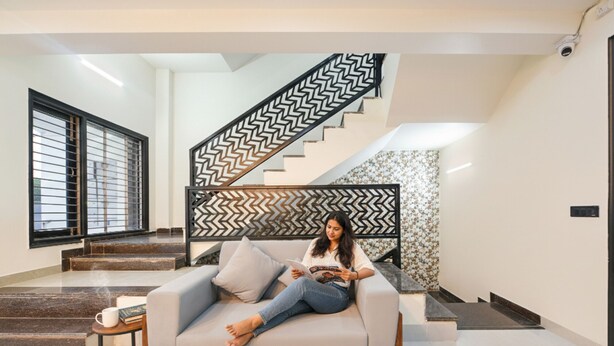A modern living room with a sofa, a coffee table, and a staircase with a geometric railing. - FabHotel RR Premium (Gurugram)