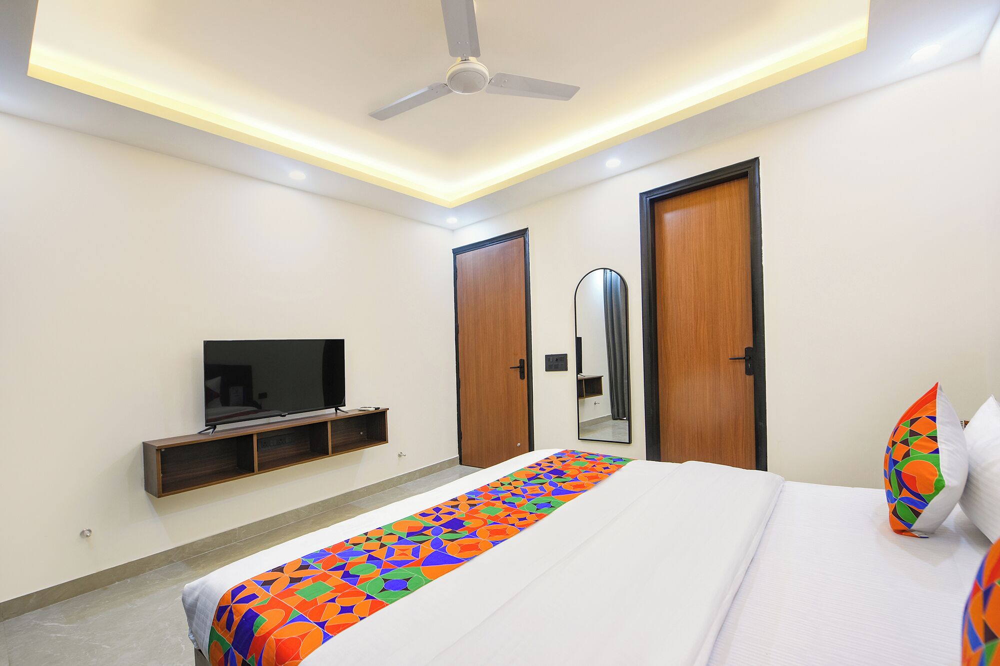 Una camera d'albergo moderna con un letto, una TV, una ventola a soffitto e uno specchio grande.
