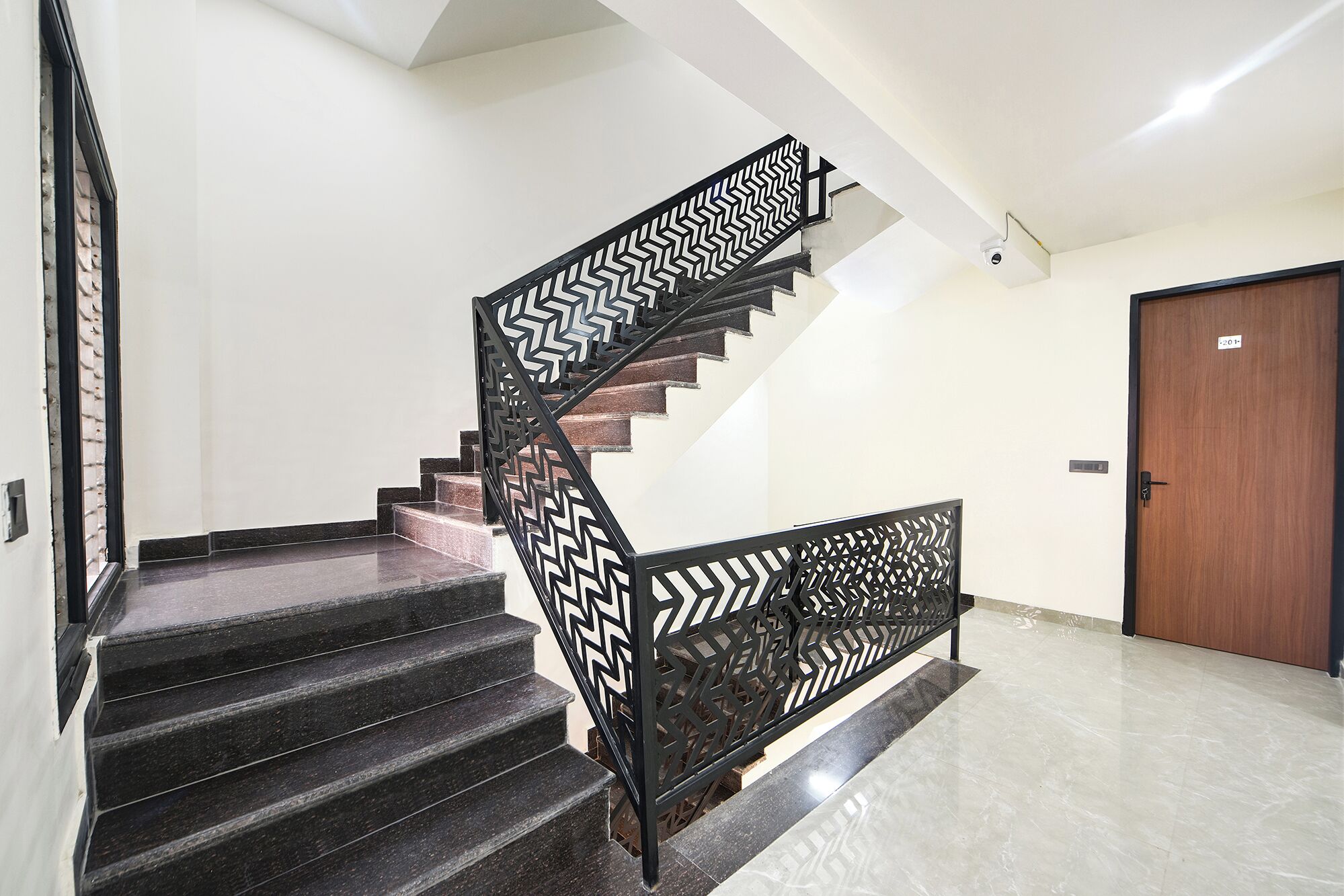 A staircase with a black metal railing featuring a geometric pattern, leading to a wooden door.