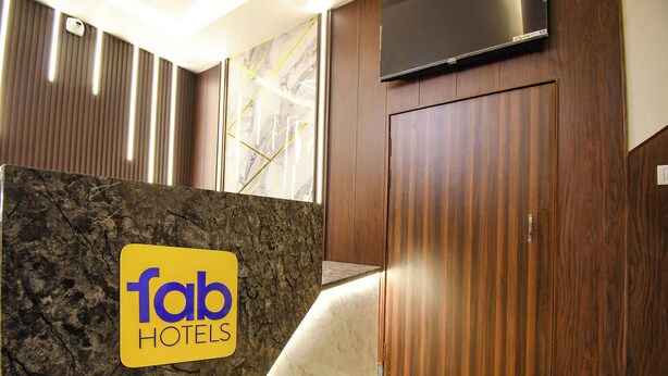 A hotel interior with a marble wall, wooden paneling, and a flat-screen TV mounted above a wooden door. - Fabhotel Jayaditya Palace (Ayodhya)