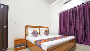 A room with a wooden bed, two pillows, a nightstand, a purple curtain, and a door. - Fabhotel Jayaditya Palace (Ayodhya)