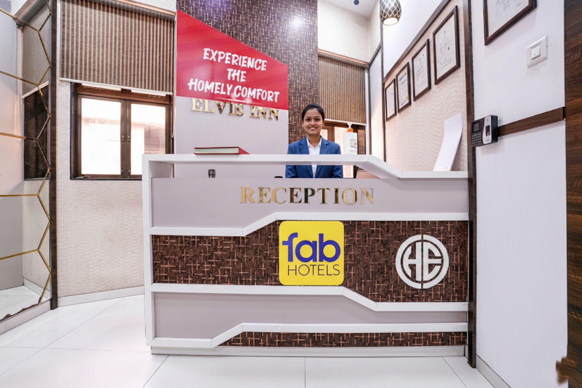 A reception desk with a sign reading "Experience the Homely Comfort of Elvis" and "Fab Hotels" logo.