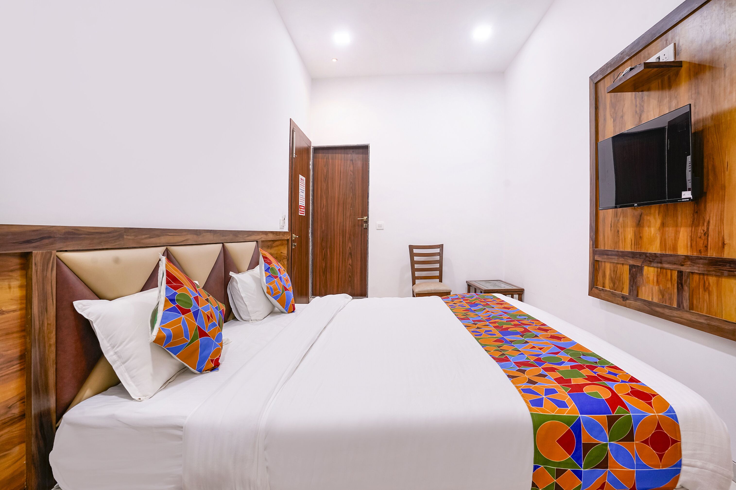 A hotel room with a bed, a TV mounted on the wall, a wooden headboard, and a door.