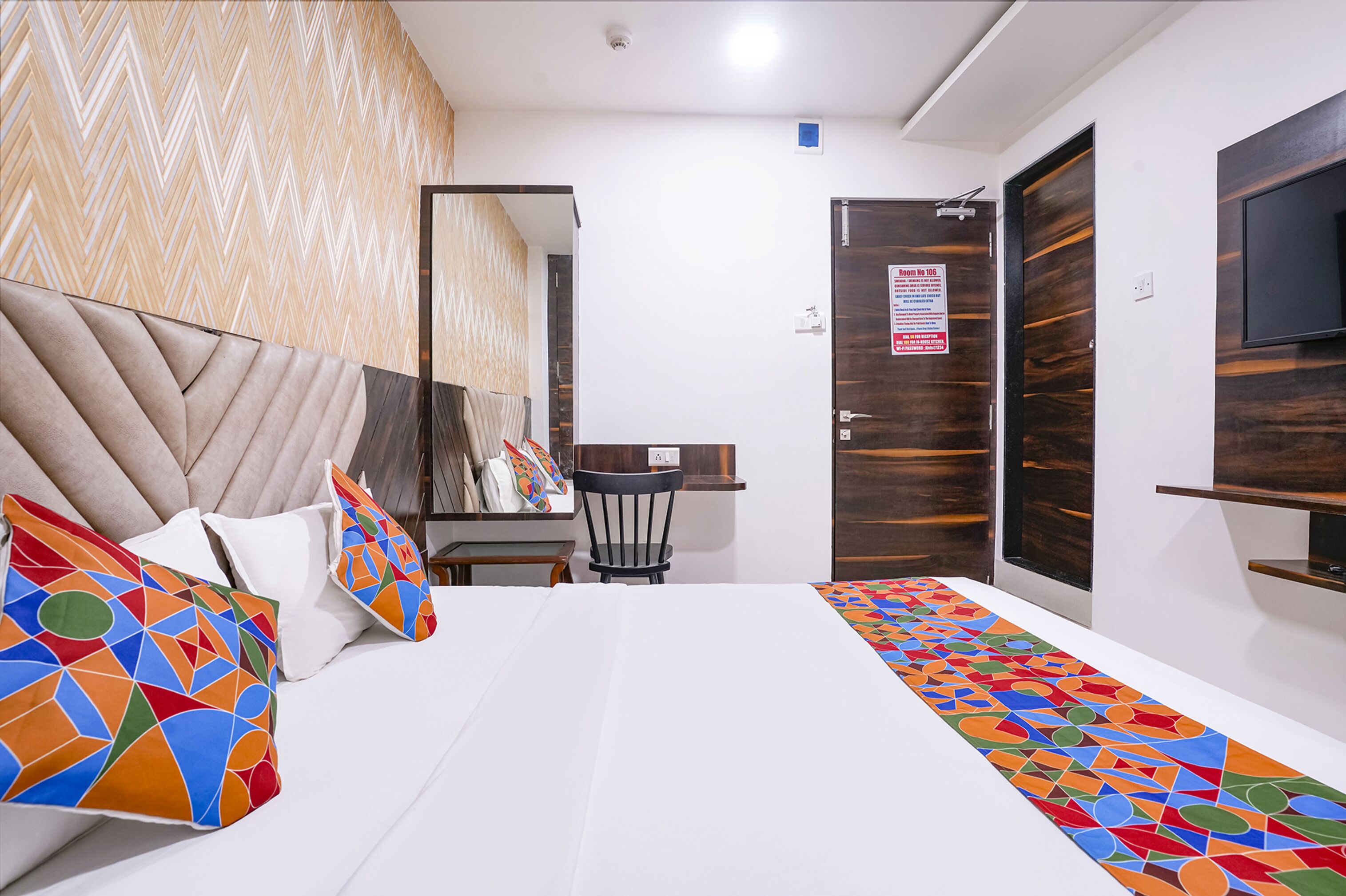 A hotel room with a bed, a chair, a desk, a TV, and a mirror.
