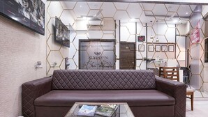Un salón moderno con un sofá de cuero marrón, una mesa de centro de vidrio con revistas y un muro con diseño hexagonal.