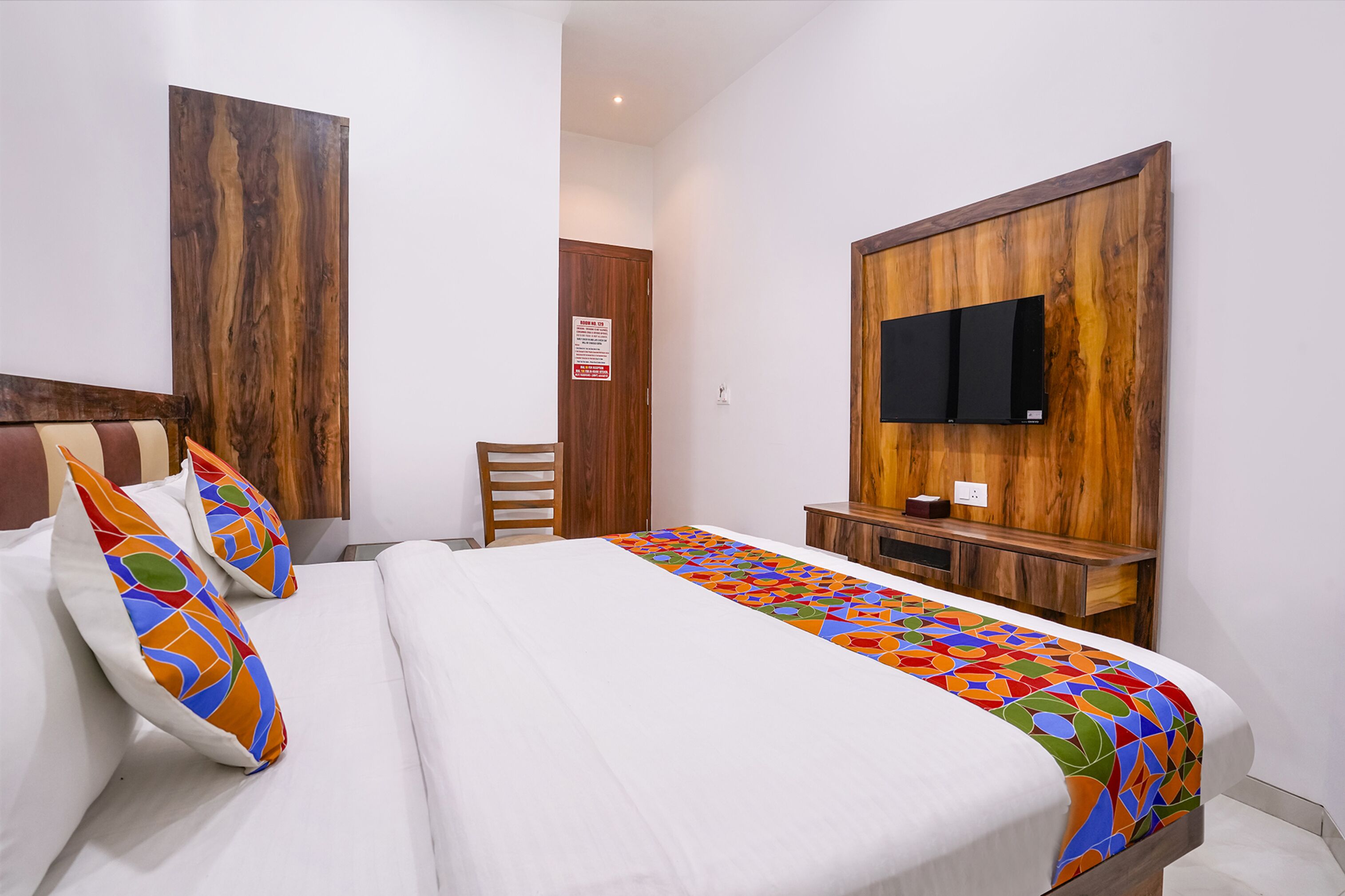 Habitación de hotel con cama, cabecera de madera, televisor montado en la pared y una pequeña mesa de madera.