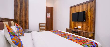 Habitación de hotel con cama, cabecera de madera, televisor montado en la pared y una pequeña mesa de madera.