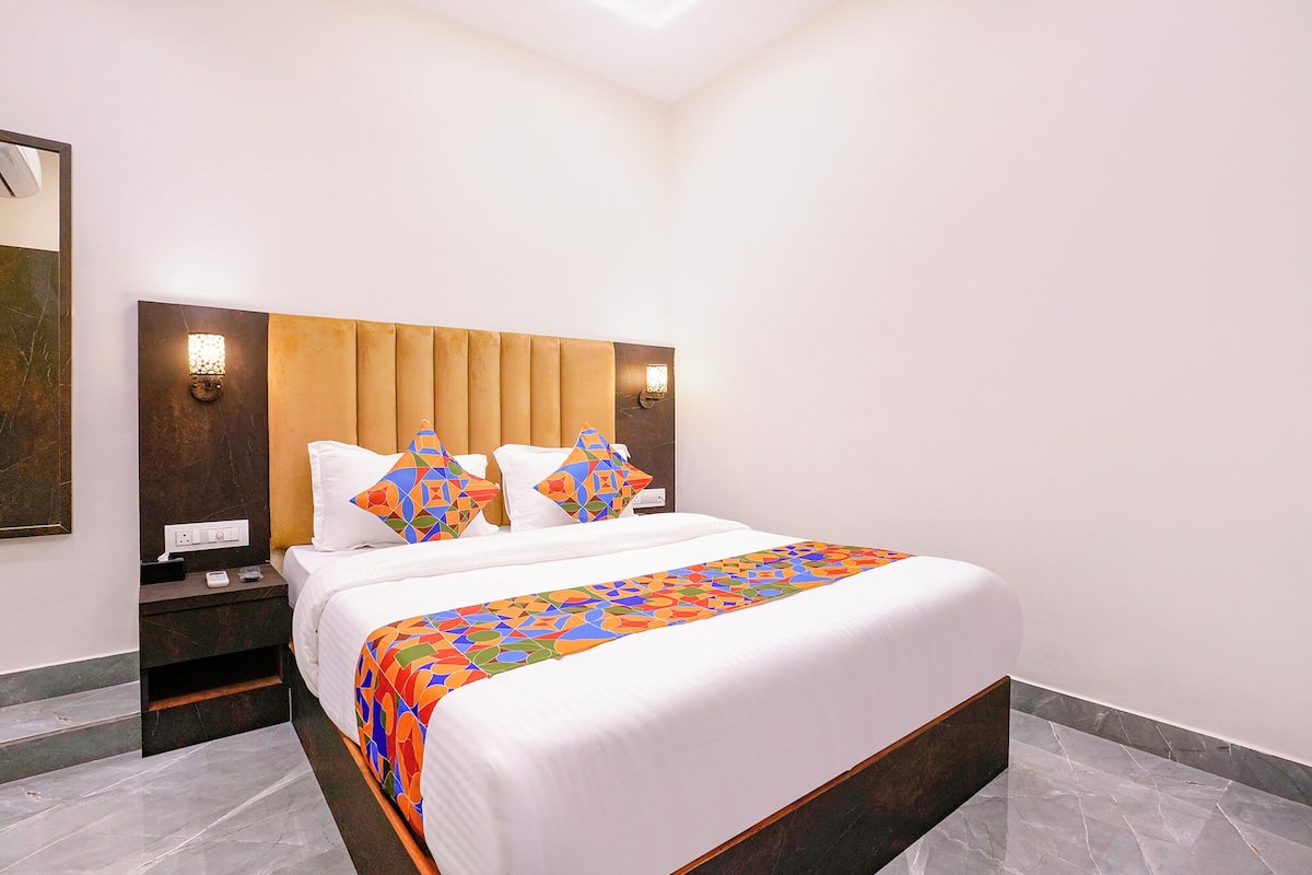A modern hotel room with a large bed, two nightstands, a wall-mounted lamp, and a patterned bed runner.