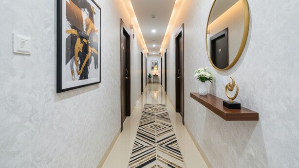 A modern hallway with a geometric patterned floor, framed artwork on the walls, a round mirror with a gold frame, and a small shelf with a decorative item. - Fabhotel Dlf Inn (Hyderabad)