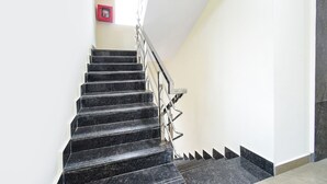A staircase with black marble steps and metal railings, leading to a landing with a fire extinguisher mounted on the wall. - Fabhotel Dlf Inn (Hyderabad)