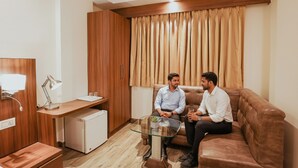 A modern living room with a brown leather sofa, a glass coffee table, and a small white refrigerator. - Fabhotel The Kailash Dev (New Delhi)
