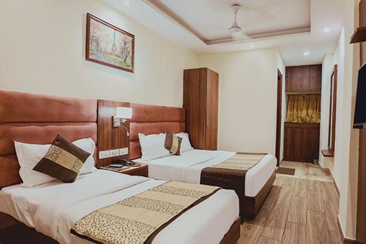 A hotel room with two beds, a wooden headboard, a nightstand, a TV, and a painting on the wall.