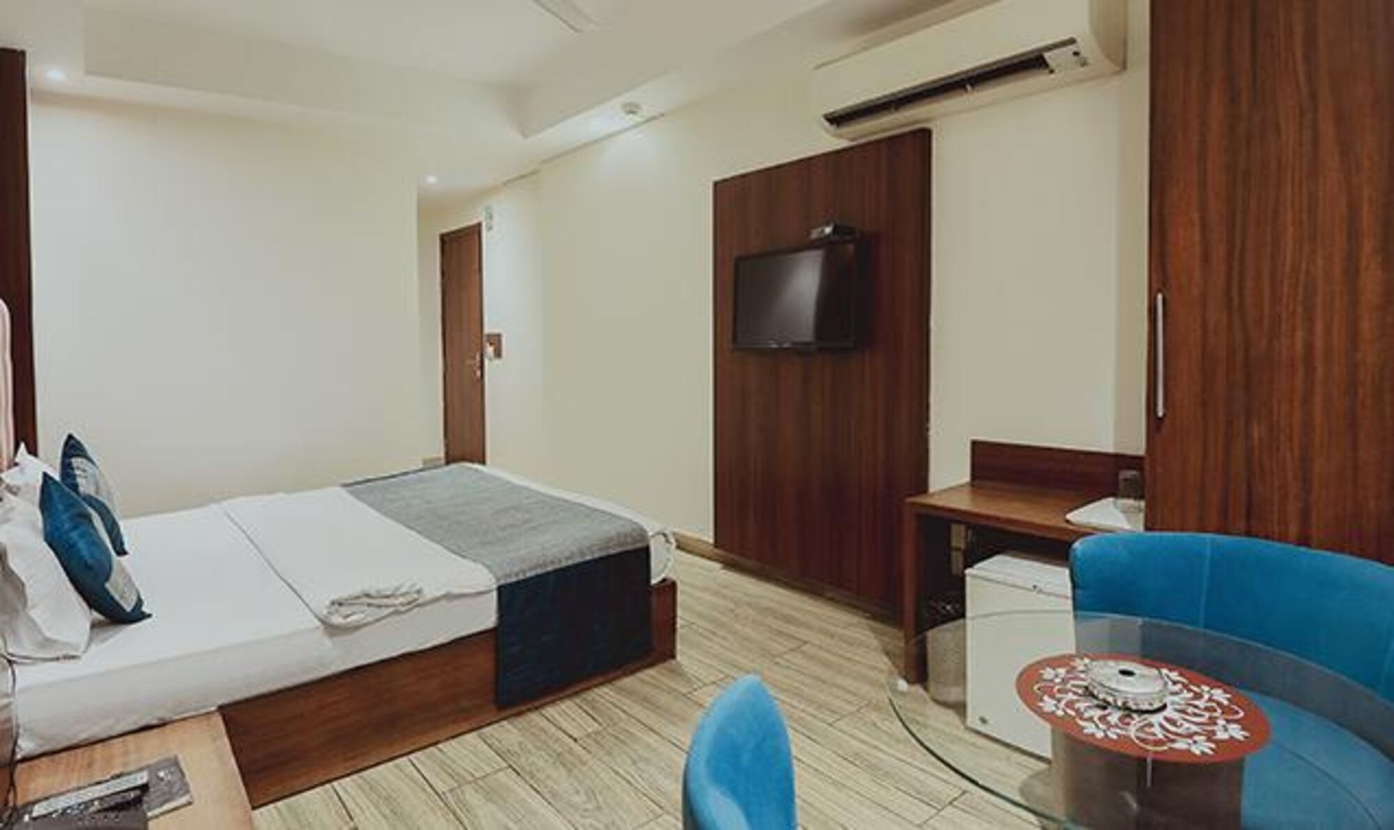 A hotel room with a bed, a desk, a chair, a TV, and a small table.