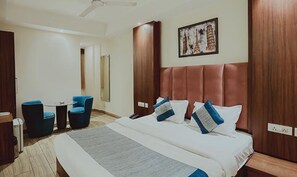 Ein Hotelzimmer mit einem großen Bett, zwei blauen Stühlen, einem kleinen Tisch und einem Bild bekannter Pariser Sehenswürdigkeiten an der Wand.