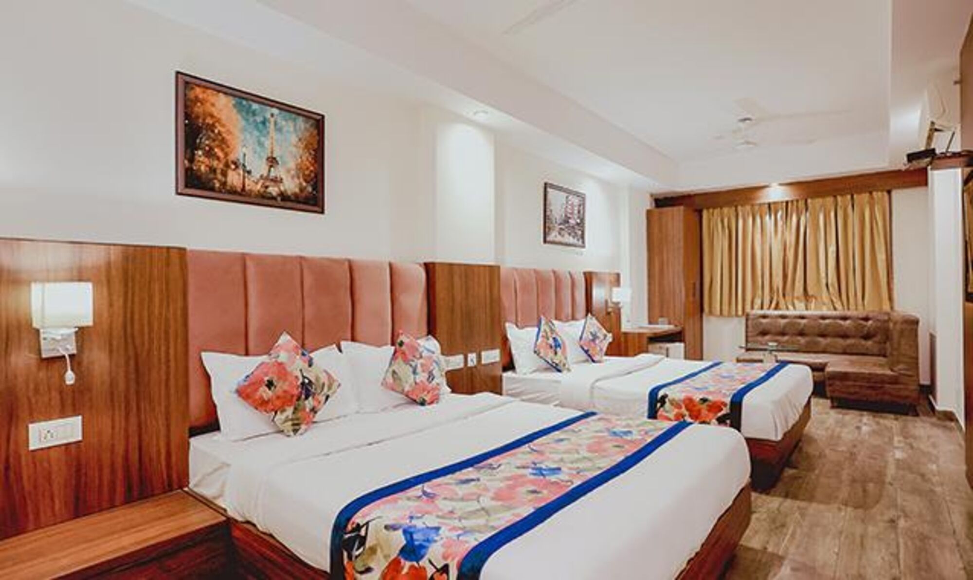 A hotel room with two beds, a sofa, and a painting on the wall.