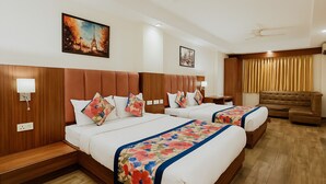 A hotel room with two beds, a wooden headboard, a sofa, and a ceiling fan. - Fabhotel The Kailash Dev (New Delhi)