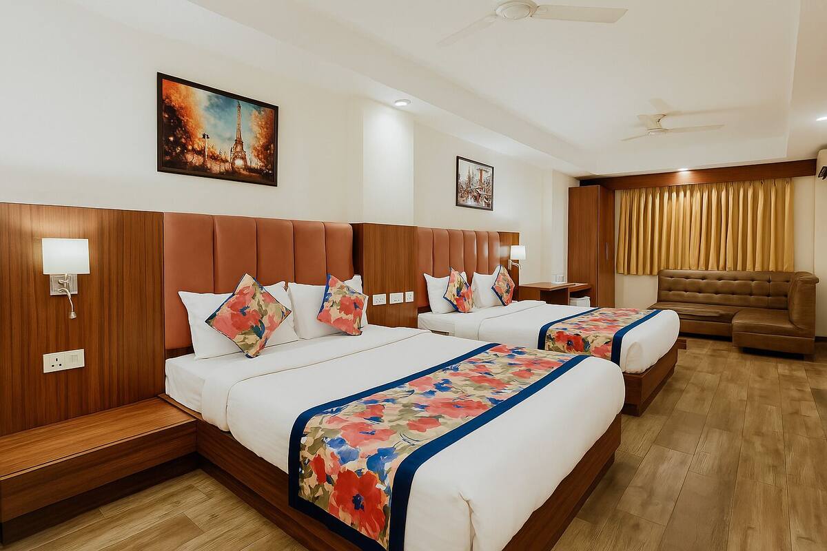 A hotel room with two beds, a wooden headboard, a sofa, and a ceiling fan.