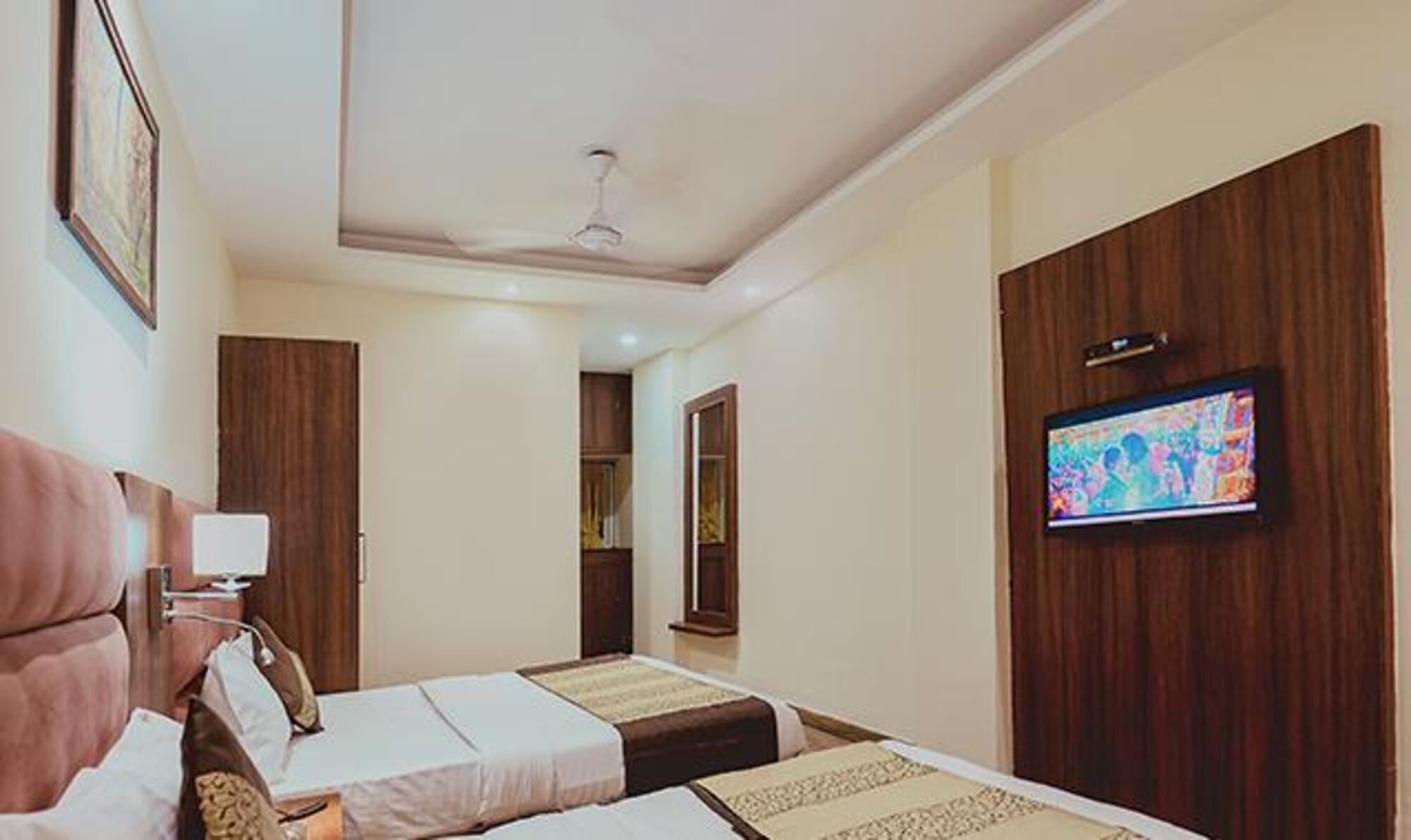A hotel room with two beds, a television mounted on the wall, and a ceiling fan.