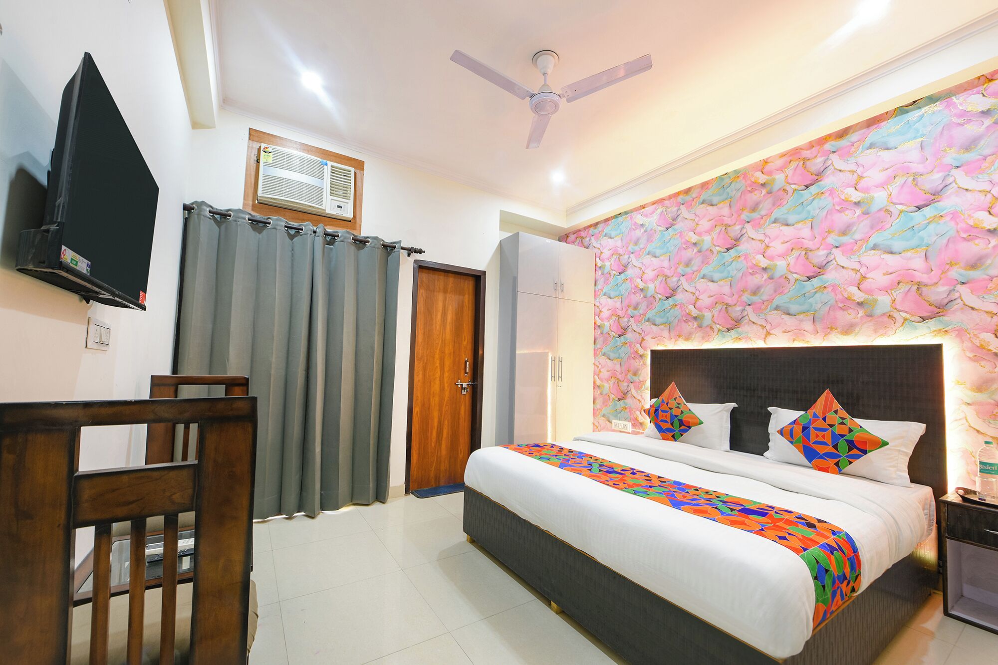 A bedroom with a bed, a desk, a chair, a wardrobe, a television, and a ceiling fan.