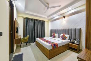 A hotel room with a bed, a chair, a bedside table, and a ceiling fan. - Fabhotel Dm 45 (Gurugram)