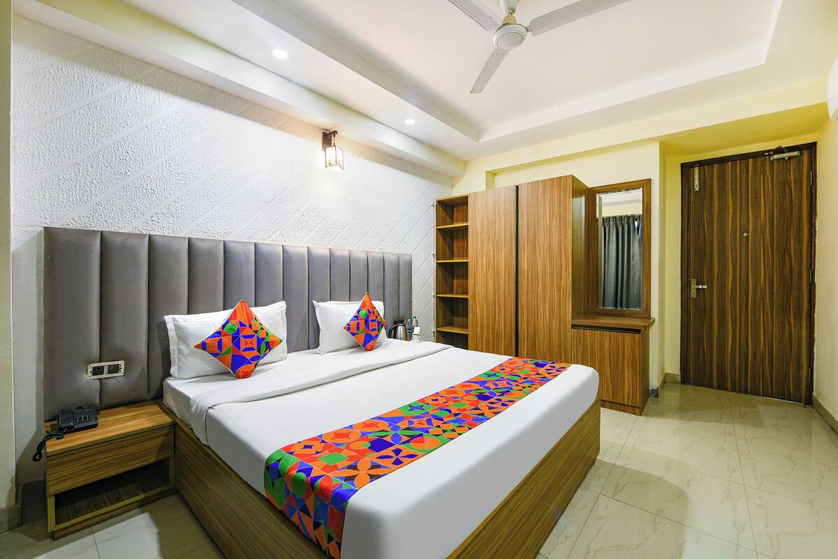 Habitación de hotel con una cama grande, un armario de madera, una mesita de noche con teléfono y un ventilador de techo.
