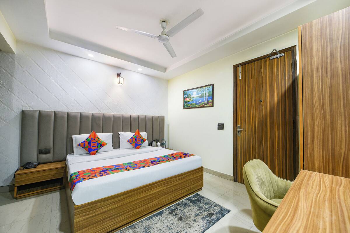 Un dormitorio con cama, mesita de noche, silla, armario de madera, ventilador de techo y un cuadro en la pared.