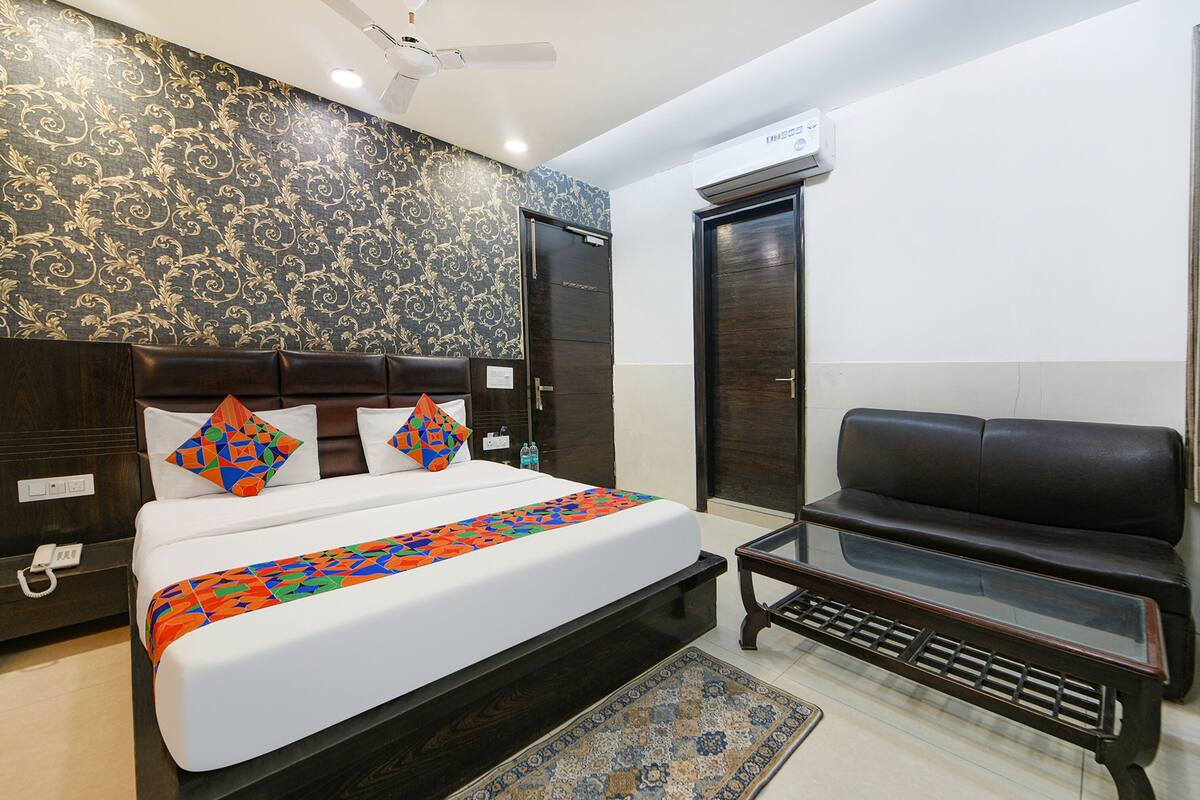 A hotel room with a large bed, a sofa, a small table, and a patterned rug.